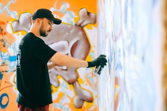 Young caucasian man graffiti artist drawing on a wall.