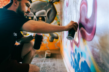 Young caucasian man graffiti artist drawing on a wall. - obrazy, fototapety, plakaty