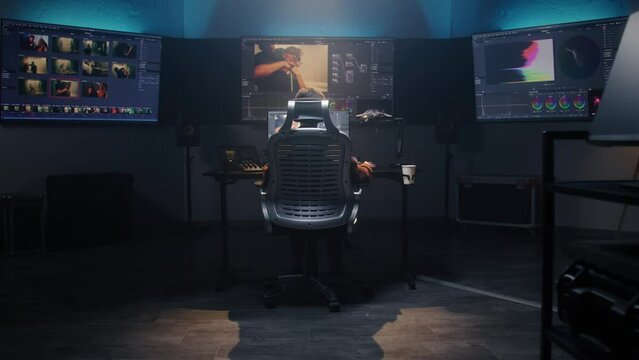 The editor works in studio on computer, edits video, makes color correction for movie post production. Big screens showing color grading program interface with film footage, RGB graphic and levels.