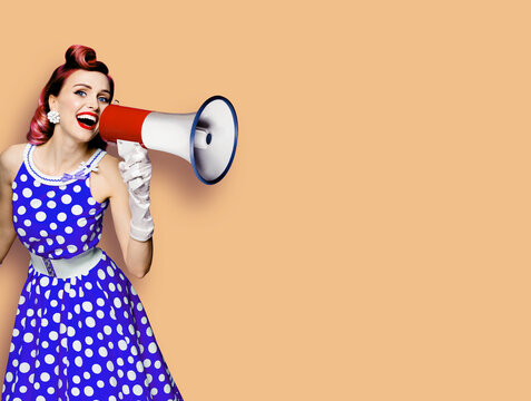 Portrait image of purple haired woman holding mega phone, shout advertise something. Girl in blue pin up style dress with mega phone loudspeaker. Isolated latte beige background. Beauty model.