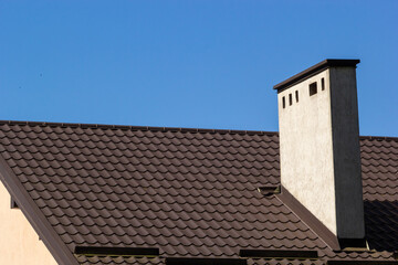 Roof of a new home. Ceramic chimney, metal roof tiles, gutters, roof window. Single family house