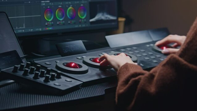 Female editor works in studio, uses digital color grading control panel. Colorist makes video color correction on computer. Program interface with RGB graphics, color wheels and levels on PC monitor.