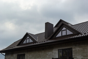 House with new brown metal tile roof and rain gutter. Metallic Guttering System, Guttering and Drainage Pipe Exterior