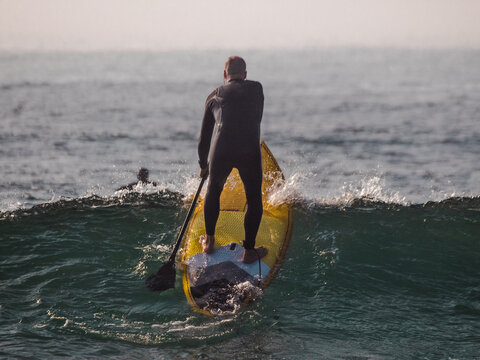 Surfer doing SUP on the sea while there are beautiful blue waves at sundown 