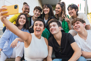 Multiethnic group of happy young friends sitting on stairs taking selfie - Diverse teenagers having fun while a break of university classes