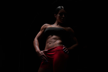 Fototapeta na wymiar Muscular woman wearing fitness clothing posing against black background. Caucasian female model with perfect abs.