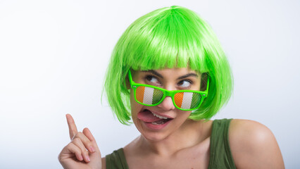 Cheerful young woman in green wig and funny glasses celebrating st patrick's day on a white...