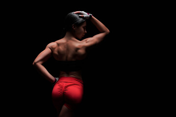Athletic young woman showing back and arm muscles on isolated black background.