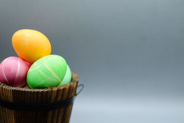 Colorful eggs in  small wooden barrel in grey background