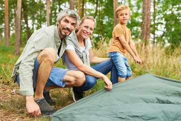 Happy parents with son setting up tent in nature