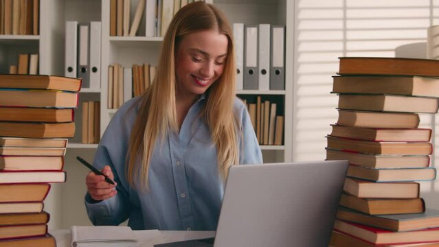 Smiling happy Caucasian student girl university leaner motivated carefree woman studying with laptop and books write homework writing learning online smile prepare for test exam study at home library