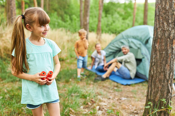 Fototapeta premium Girl holding binoculars with family sitting in background