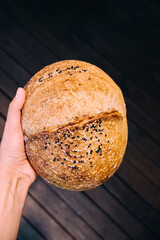 Female hand holding homemade sourdough bread. Freshly baked with seeds. 