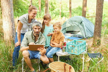 Man sharing digital tablet with family at campsite