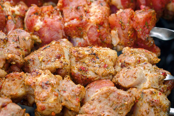 Meat cooked at barbecue and raw sticks  on background, close up. Shish kebab cooking outdoors. Raw spicy marinated meat cook on bbq grill. Pork meat, shashlik, prepared on grill wood coal, outdoor