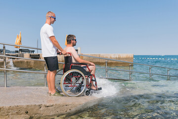 Man with disability on wheelchair at accessible beach goes swimming.