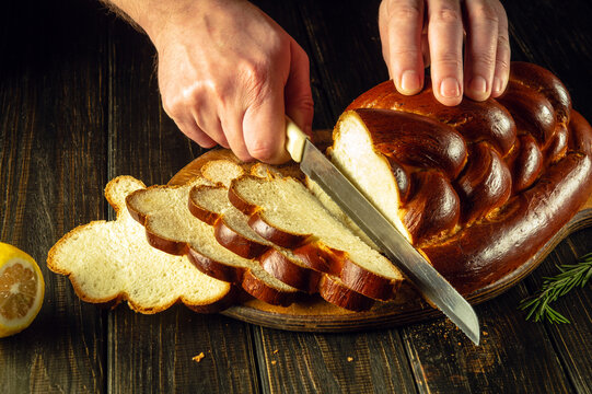 Cook's hands cut with a knife fresh bread or kolach on a kitchen cutting board for lunch. Healthy food and traditional bakery concept