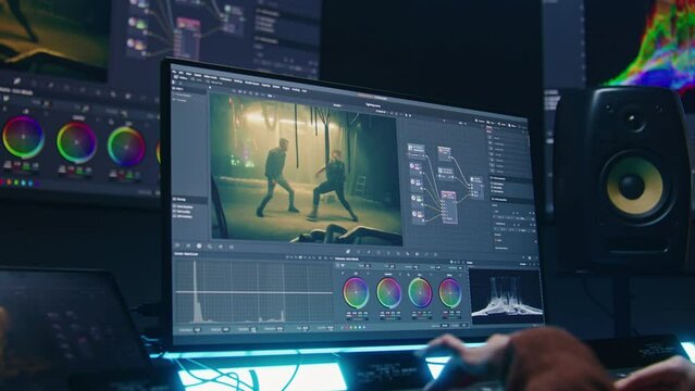 Female colorist uses color grading control panel, edits video, makes film color correction on computer in studio. Movie footage and RGB wheels on monitor. Big screens and tablet with program interface