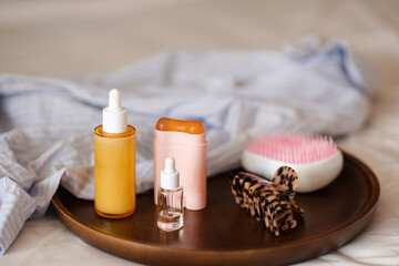 Beauty products stay on wooden tray with home clothes shirt in bed close up. Skin care routine.