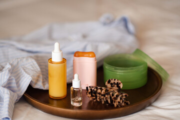 Beauty products stay on wooden tray with home clothes shirt in bed close up. Skin care routine.