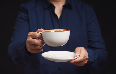 Close-up of hands holding a coffee cup against a black background