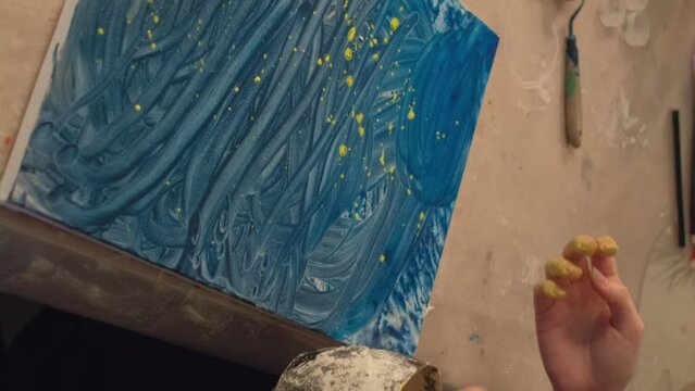 Vertical video. Kid painting. Art class. Bonding leisure. Mother little child hand fingers sprinkling blue color abstract artwork with yellow paint.