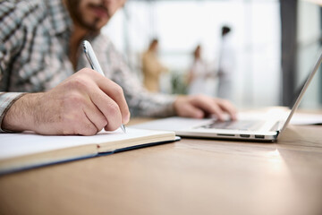 Fototapeta premium male hands writes a pen in a notebook, computer keyboard in background.