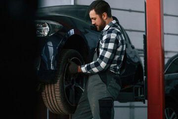 Fototapeta na wymiar Holding and changing new tire. Man in uniform is working in the auto salon