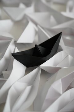 Unique black paper origami ship among white ones