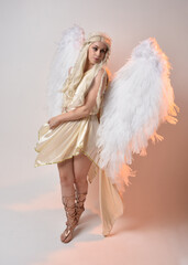 Full length portrait of beautiful blonde woman wearing a fantasy goddess toga costume with feathered angel wings. 
 Jumping pose like flying, isolated on white studio background.