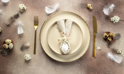 Easter brunch table setting. Easter egg in bunny napkin on plate with cutlery, bunny, spring flowers. Long banner format. top view