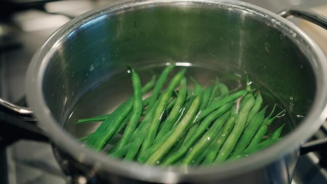 A close-up view of vibrant green beans starting to boil in a steaming pot. Cooking vegetarian and healthy eating concept.