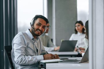 Man is sitting in front of his colleagues. Four people are working in the office together