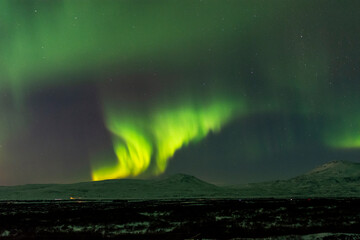 imagen de un paisaje nocturno nevado, con montañas de fondo, y una aurora boreal sobre el cielo de Islandia 