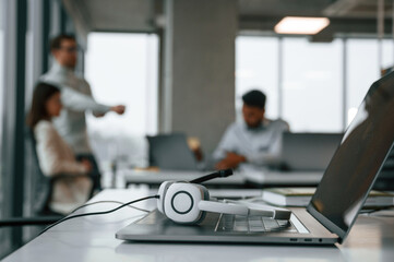 Fototapeta premium Headphones is lying down on the laptop. Men and woman are working in the office together