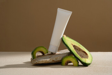 A stone with a white tube placed on, arranged with Avocado slices on beige background. Cosmetic product extracted from Avocado (Persea americana) effectively moisturize your skin