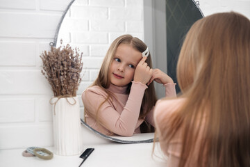 Cute teenager girl child with long blonde hair smiling looking in the round mirror, preening,...