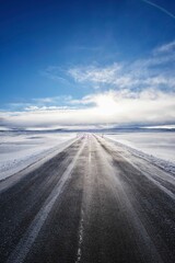 Long empty road surrounded by snow-covered fields on a sunny day in Iceland