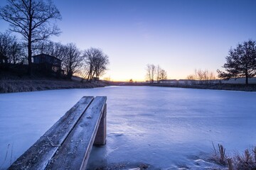 Beautiful shot of a frozen white pond with a wooden dock in the winter