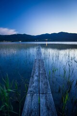 Vertical shot of a narrow wooden pier in the lake against the mountains in the Alps