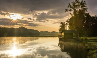 Fototapeta premium Scenic pond with a lonely hut on the shore and a beautiful sunset skyscape in the background