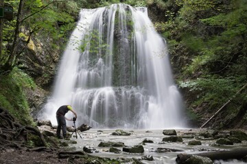 Rushing waterfall in the forest with a photographer capturing the view