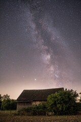 Fototapeta na wymiar Vertical shot of the Milky Way and the starry sky over a small rural house