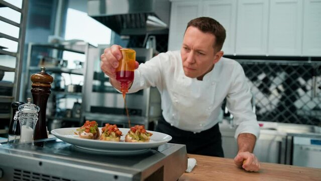 Professional chef puts avocado and tomato on toast with spices pouring sauce over it concept of healthy food breakfast 