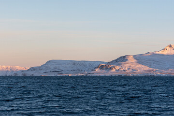 imagen de un paisaje con montañas nevadas, el cielo azul despejado y el mar