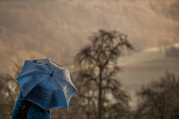Unkenntliche Person unter Regenschirm bei strömendem Regen vor kahlem Baum