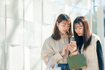 スマホを見ながらショッピングをする友達同士の若い日本人女性