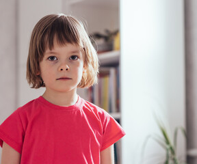 Girl in a pink t-shirt looking at the camera at home in the room. The concept of peace and security at home