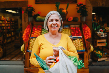 Zero waste food retail - Happy senior woman holding reusable bag of fresh vegetables at local...