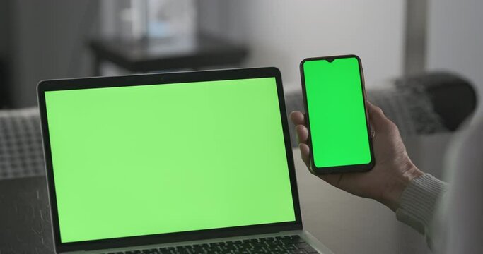 Two green screens on laptop and phone. Woman's hands are holding smartphone with chromakey. Concept of online applications, cross-platform, layout, displaying information on different devices.